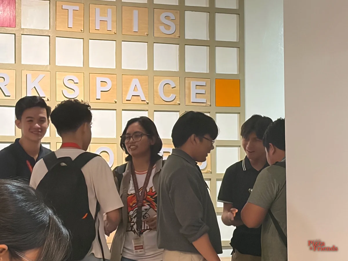 Attendees chat and laugh in a group in front of a lettered "WORKSPACE" wall.